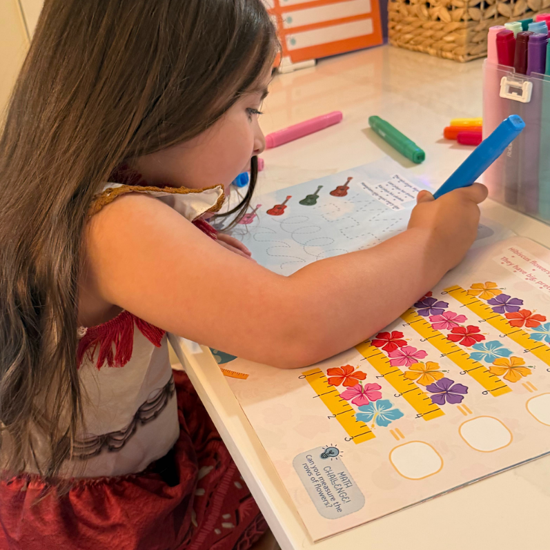Child coloring at a table with crayons and a Moana-themed dress