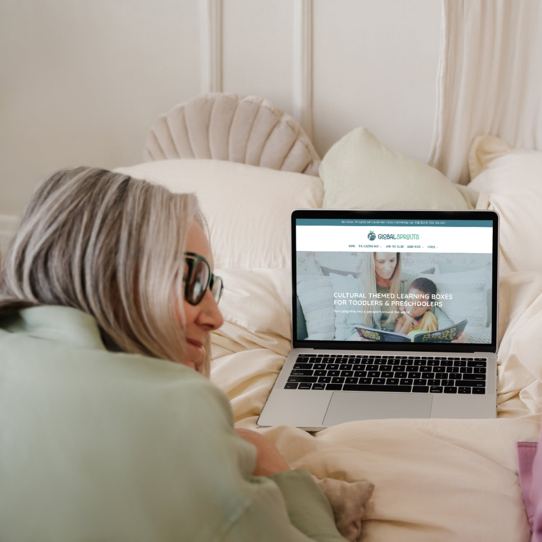Woman using a laptop on a bed with Global Sprouts website displayed on the screen