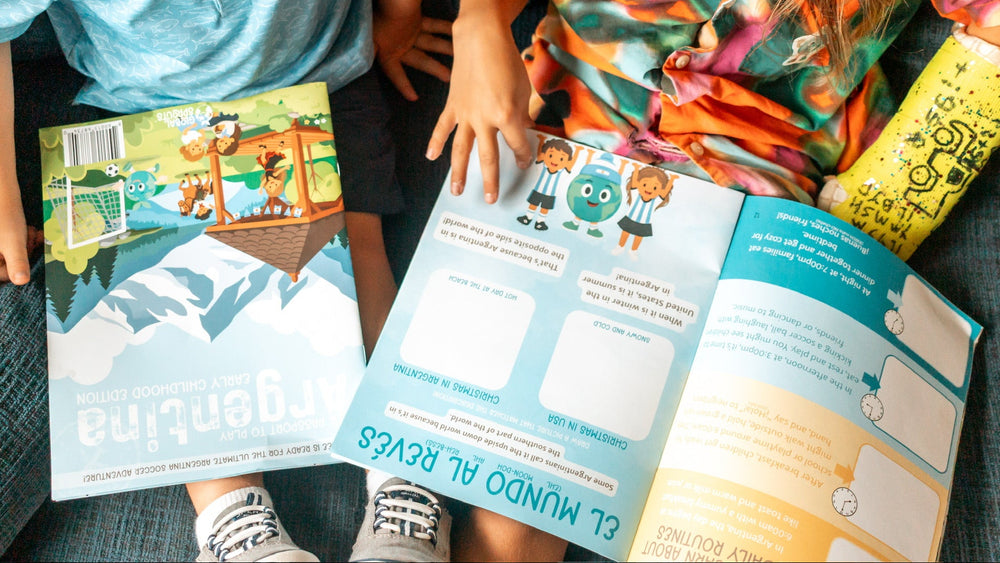 Two children sitting on a blue couch reading colorful Spanish-language books. One child holds an open book with blue and white pages, and the other holds a book with a mountain illustration.