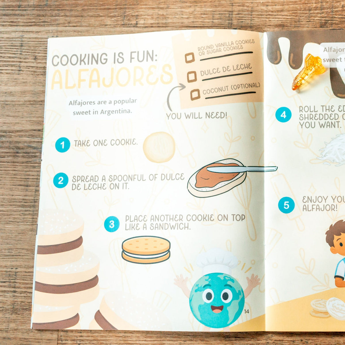 An open children's cooking book spread on a wooden surface, featuring illustrated steps for making alfajores with colorful drawings, photos of cookies, and cartoon characters.
